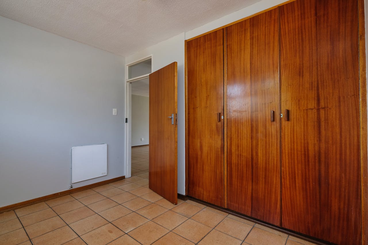 Spacious minimalist room with wooden wardrobe and open door in Pretoria, South Africa.