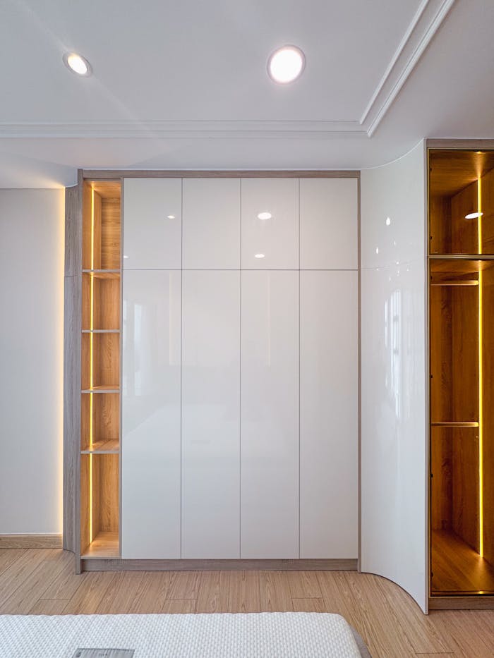Stylish modern white wardrobe with built-in lighting in a minimalist bedroom setting.