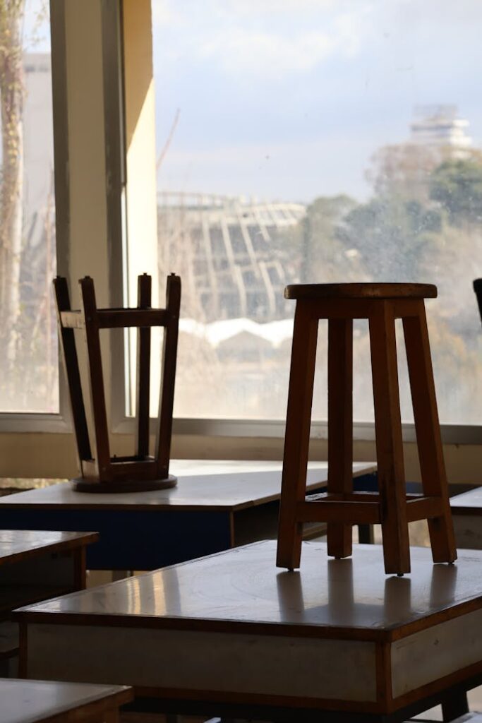 Empty classroom in Damascus with wooden stools and a view outside.